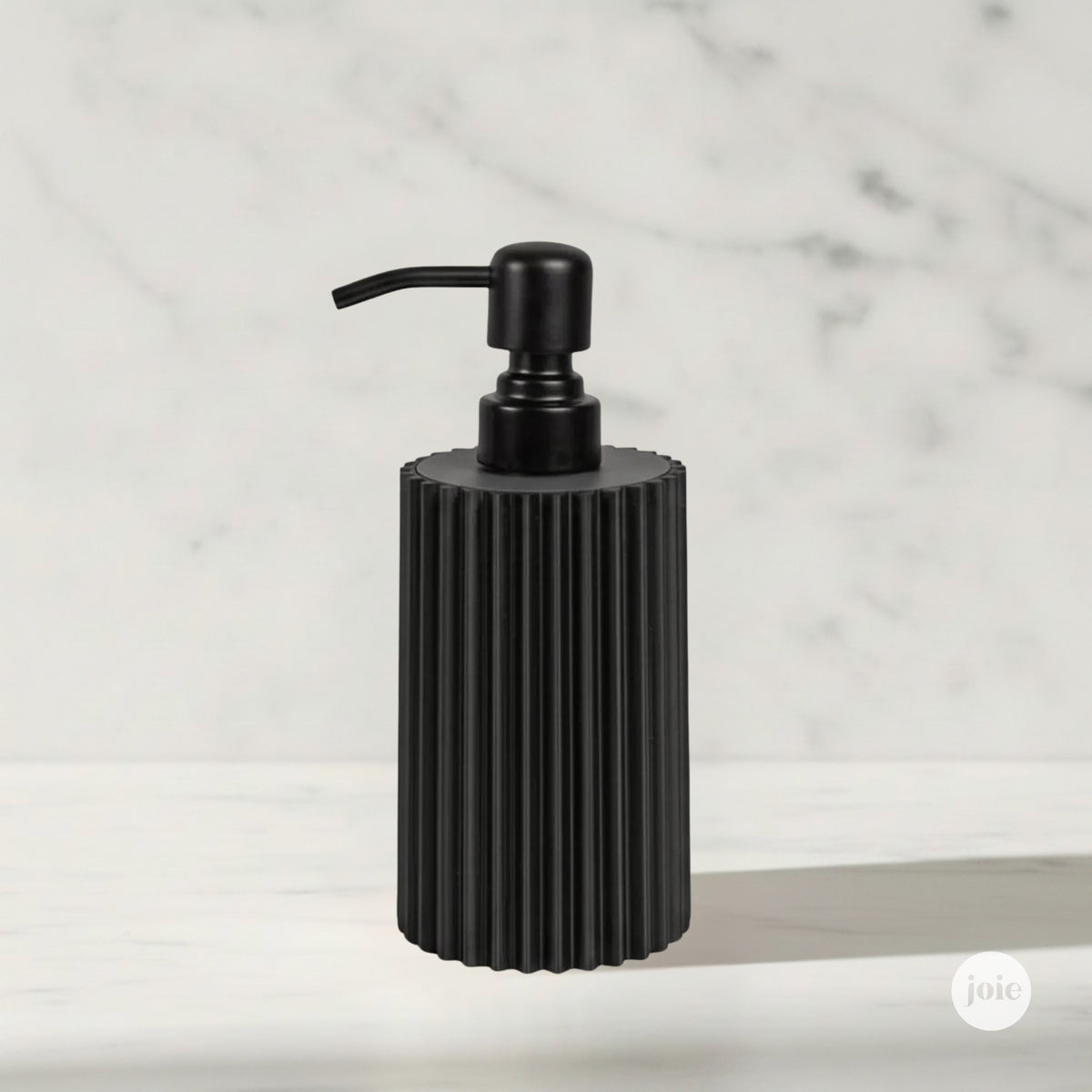 A matte black ribbed cylindrical pump dispenser with matte black metal pump stands on a white marble surface against a white marble background.