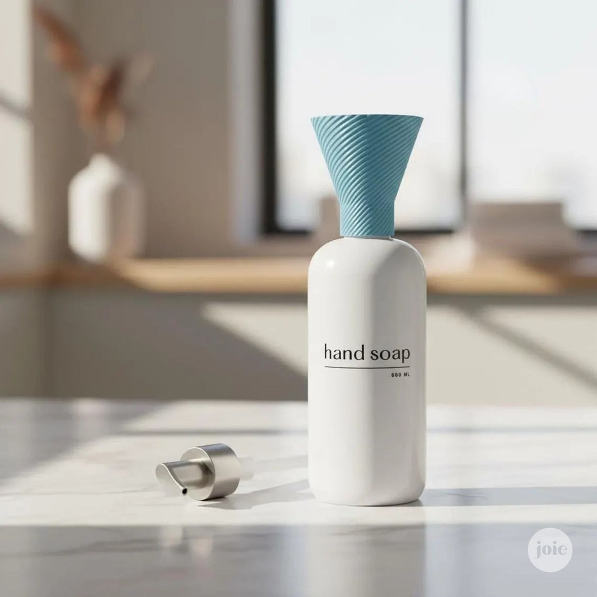 A white hand soap bottle with a light blue ribbed funnel-shaped cap stands on a light marble surface, with its silver pump dispenser placed beside it. The background is a softly blurred modern interior with warm sunlight and neutral tones.