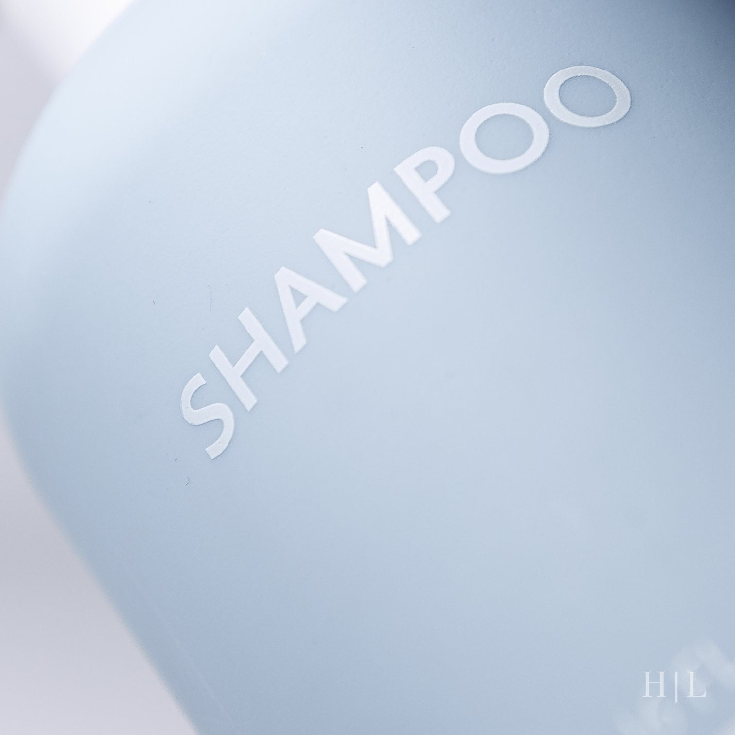 a close up of a light blue bottle of shampoo with white printed lettering