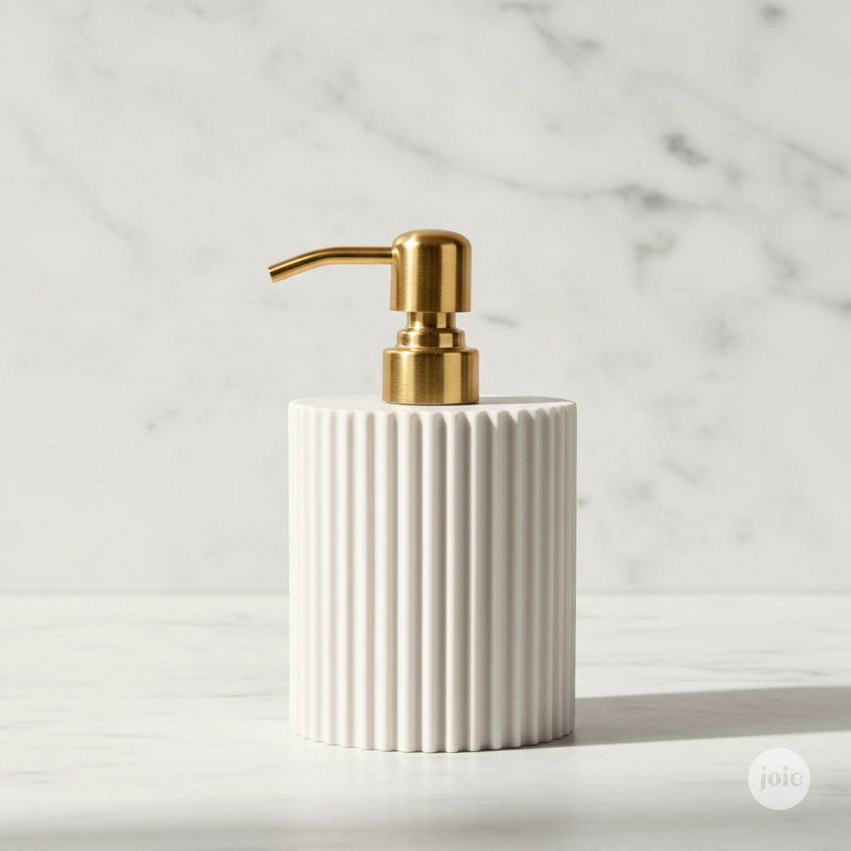 A ribbed white ceramic soap dispenser with a polished gold pump, set against a light marble background.