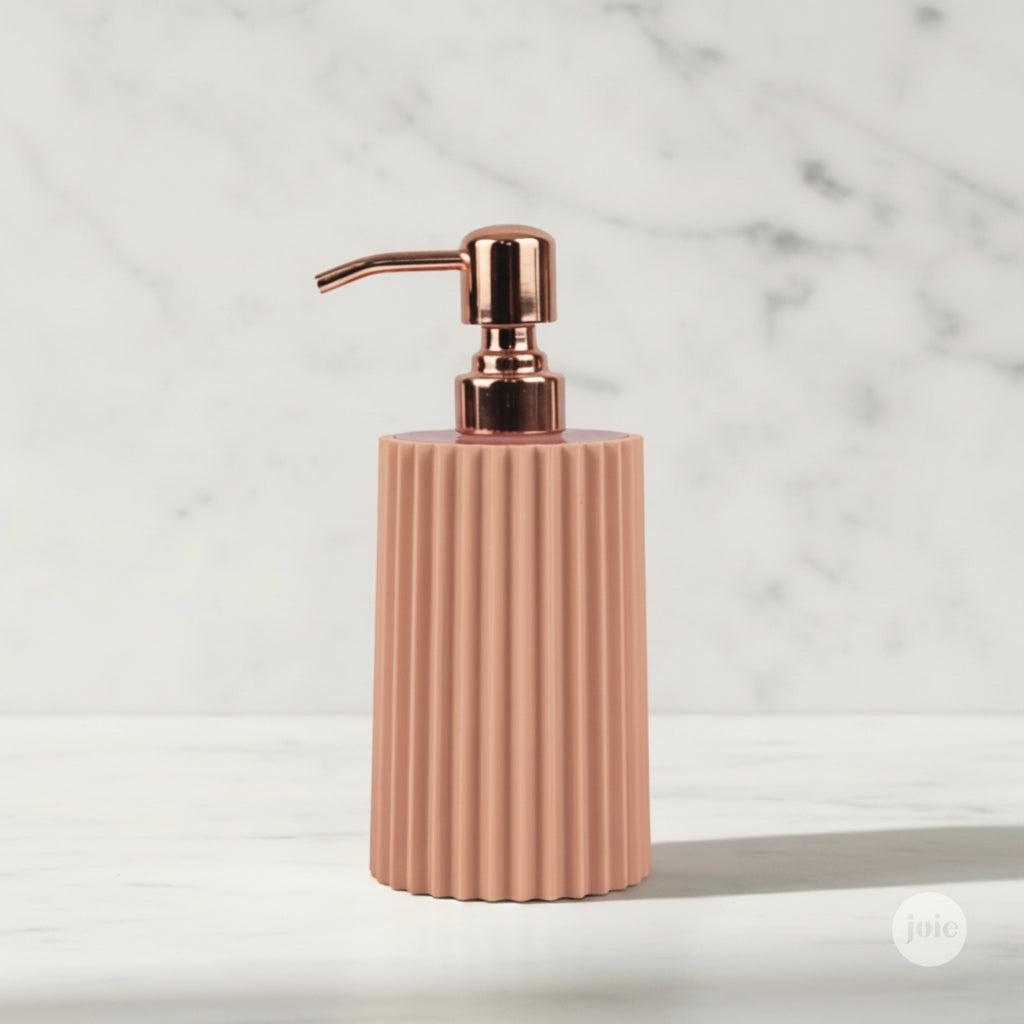 A ribbed ceramic soap dispenser in a dusty rose pink color with a metallic rose gold pump, set against a white marble background.