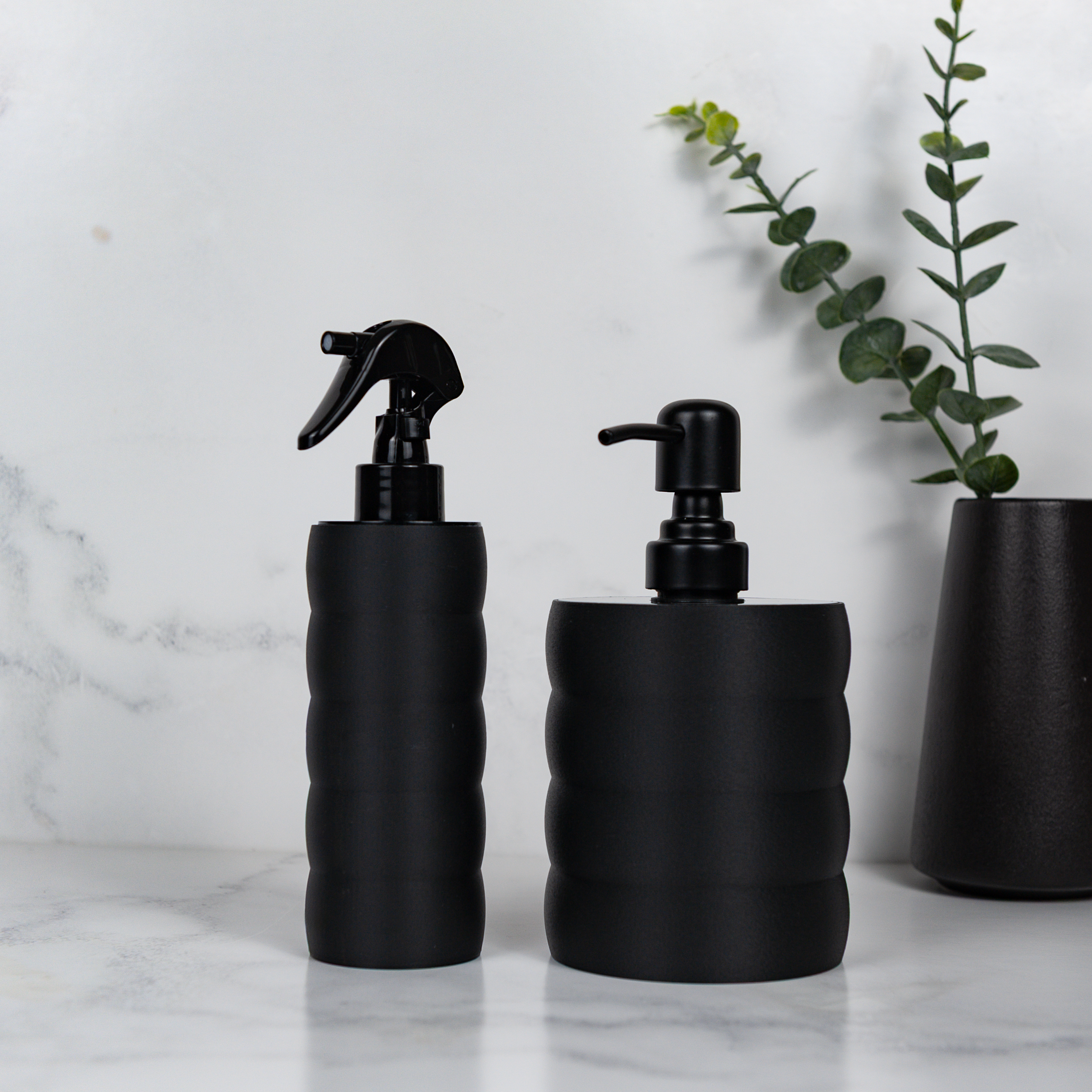 Two black textured bottles with different dispensers on a marble surface.