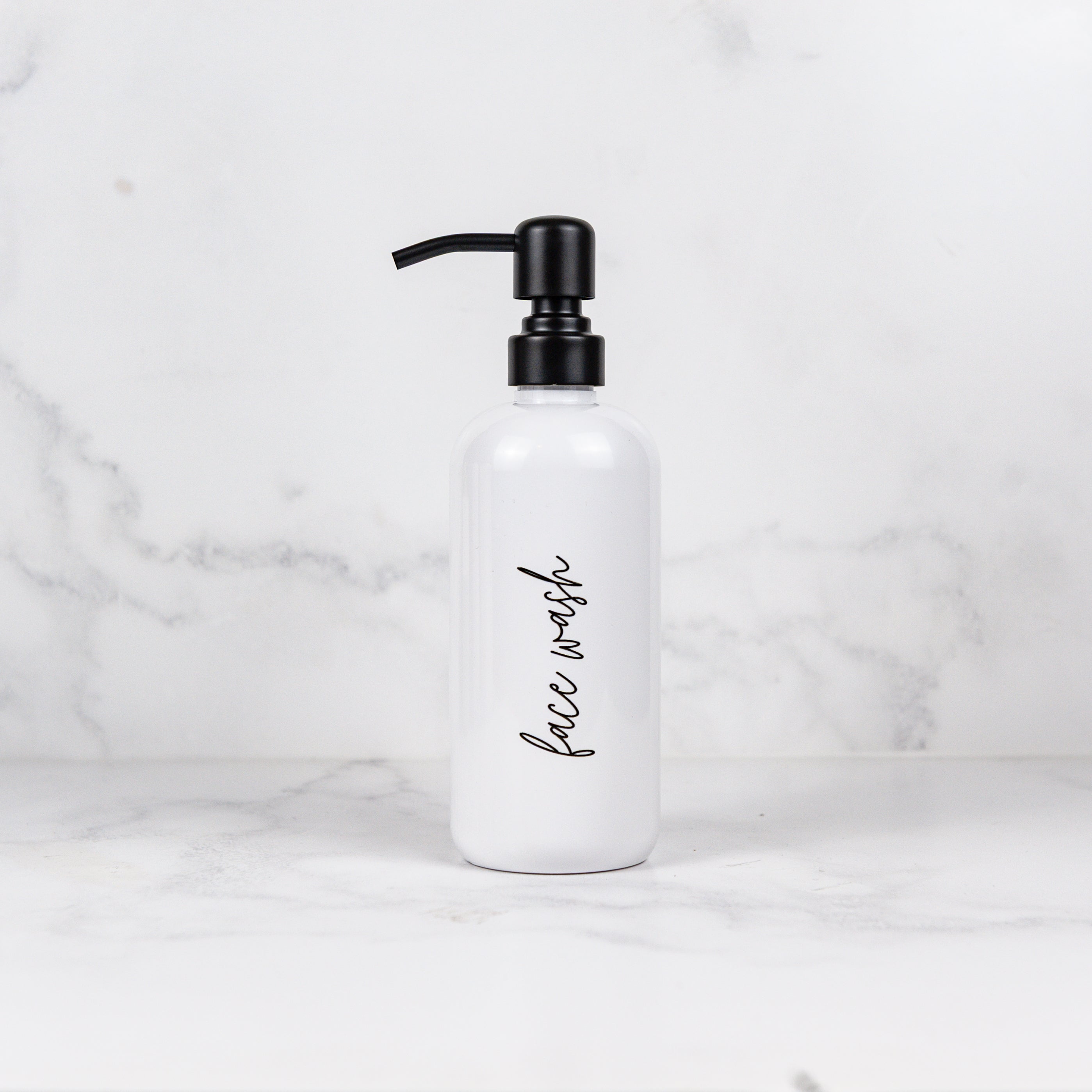 White bottle with black pump labeled 'face wash' on a marble background
