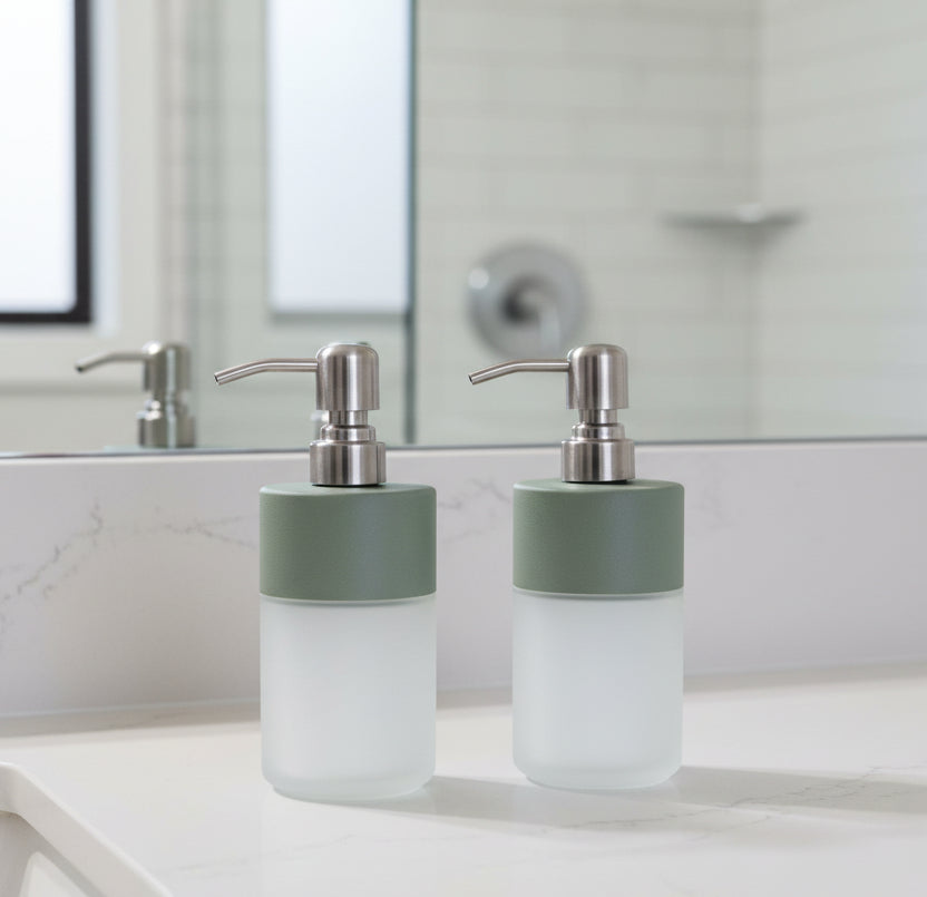 A modern soap dispenser with a frosted glass bottle, a matte sage green collar, and a brushed silver metal pump, shown on a clean white background.